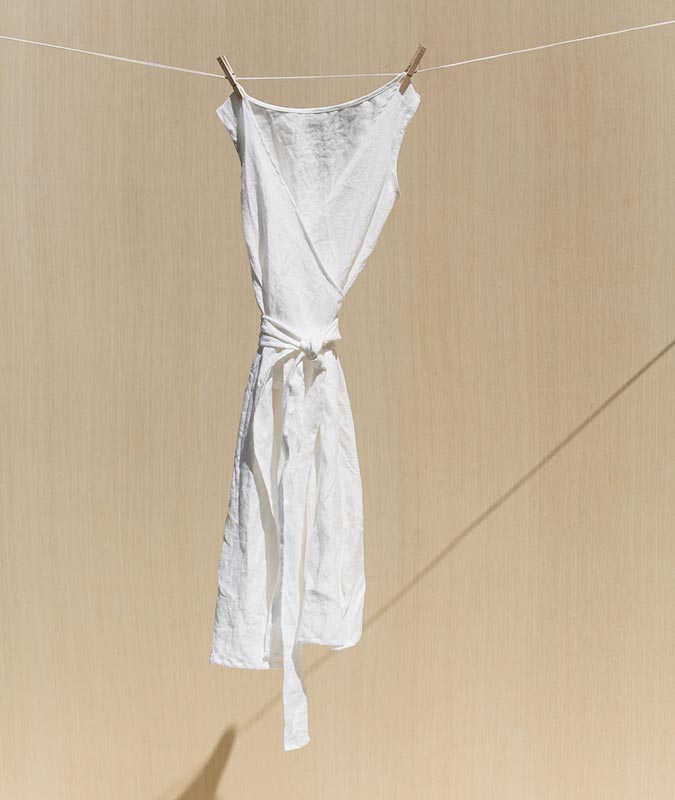 The Kayo wrap dress in ivory linen hanging from a clothesline