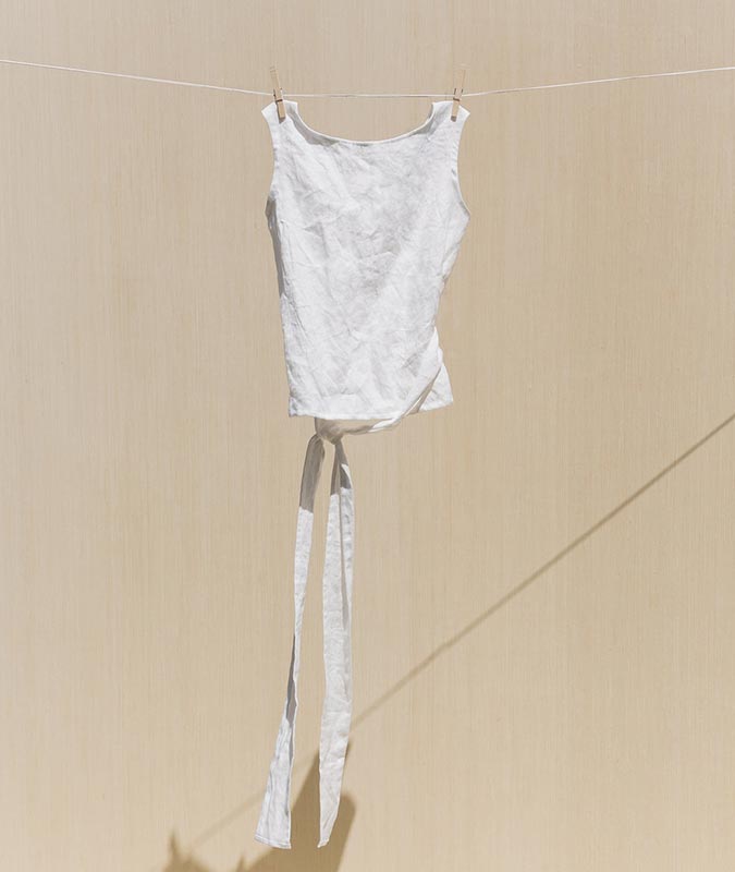 The Misakp Wrap Top in ivory linen hanging from a clothesline.