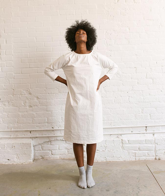woman wearing the rebecca dress, a modern baggy dress, in a natural white color