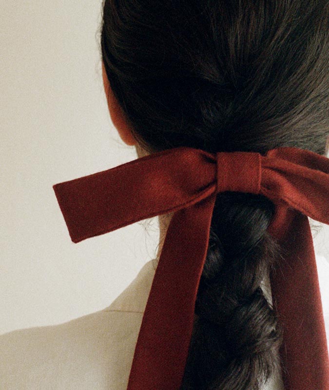 Photo of the skinny large bowtie in crimson holding a low, braided ponytail on a womans head