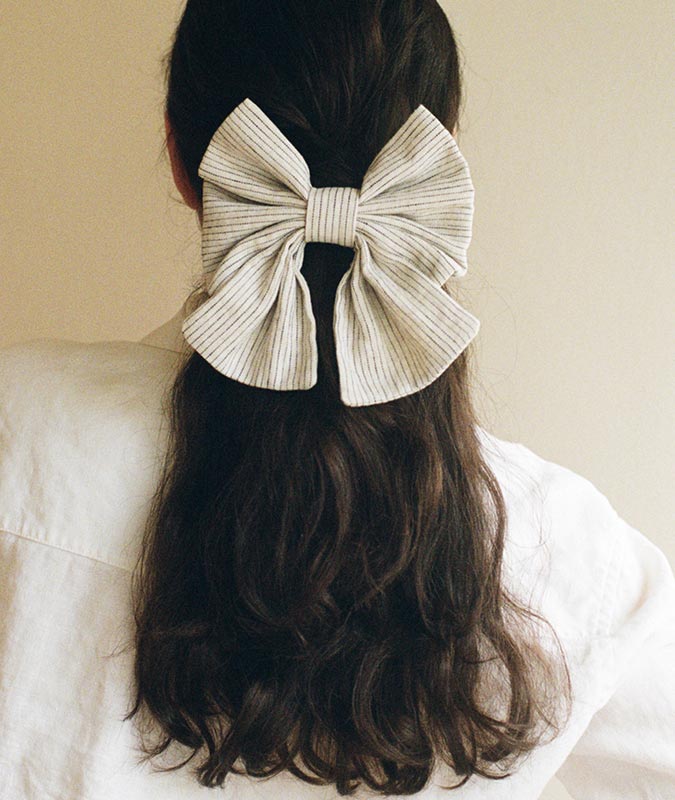 Photo of the wide small bowtie in striped linen holding a low, loose ponytail on a womans head